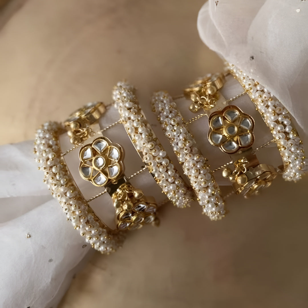 Gold-plated Kundan pearl bangles set for women with floral motifs, faux pearl beadwork, and hanging jhumki charms.