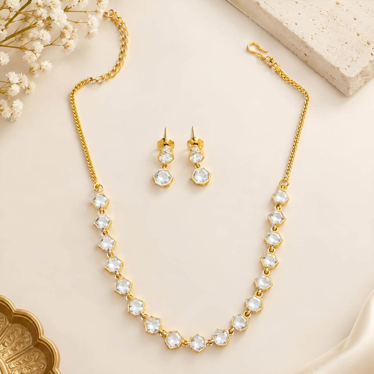 Gold plated hexagon zircon necklace set with matching drop earrings on a cream background