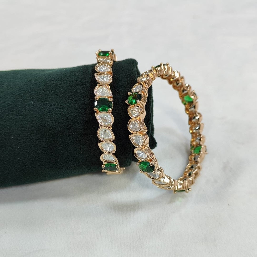 Set of gold-plated bangles with tear-drop shaped white Kundan stones and green accents displayed on a green velvet roll.