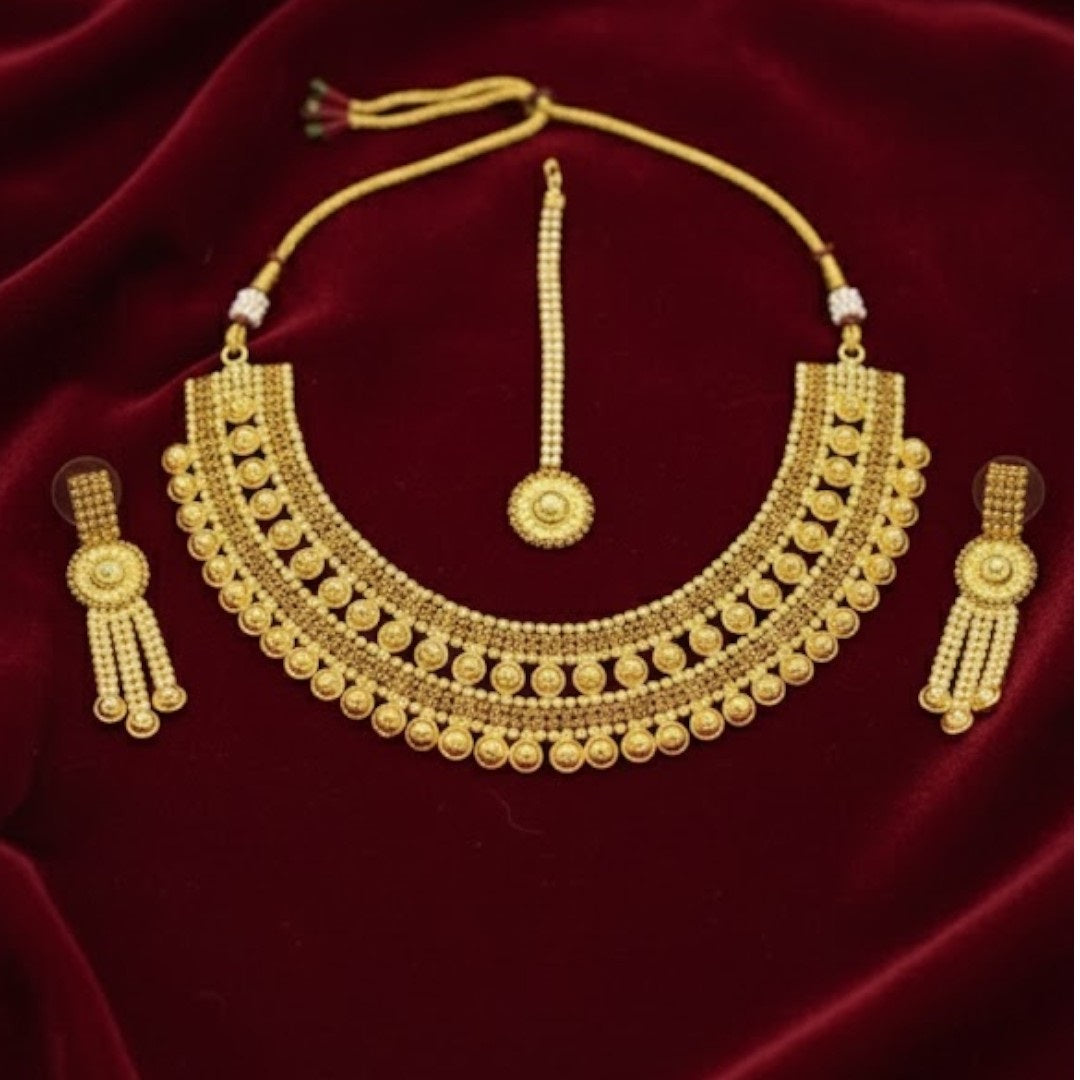 Traditional bridal gold-plated Kundan necklace set with matching earrings and maang tikka displayed on red velvet stand.