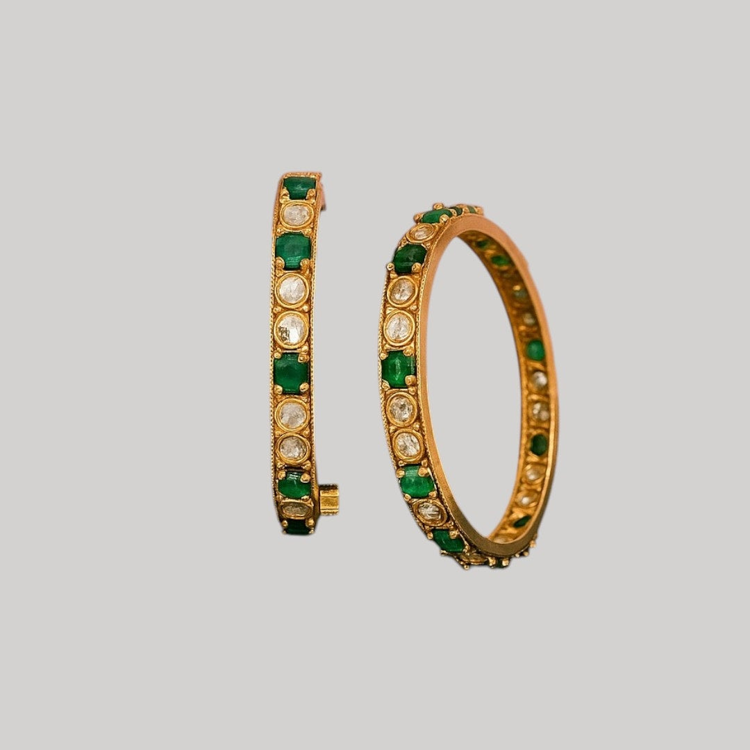 Set of gold-plated bangles adorned with alternating green and white Kundan stones, displayed on a dark green velvet roll against a white background.