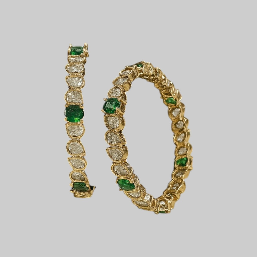 Set of gold-plated bangles with tear-drop shaped white Kundan stones and green accents displayed on a green velvet roll.