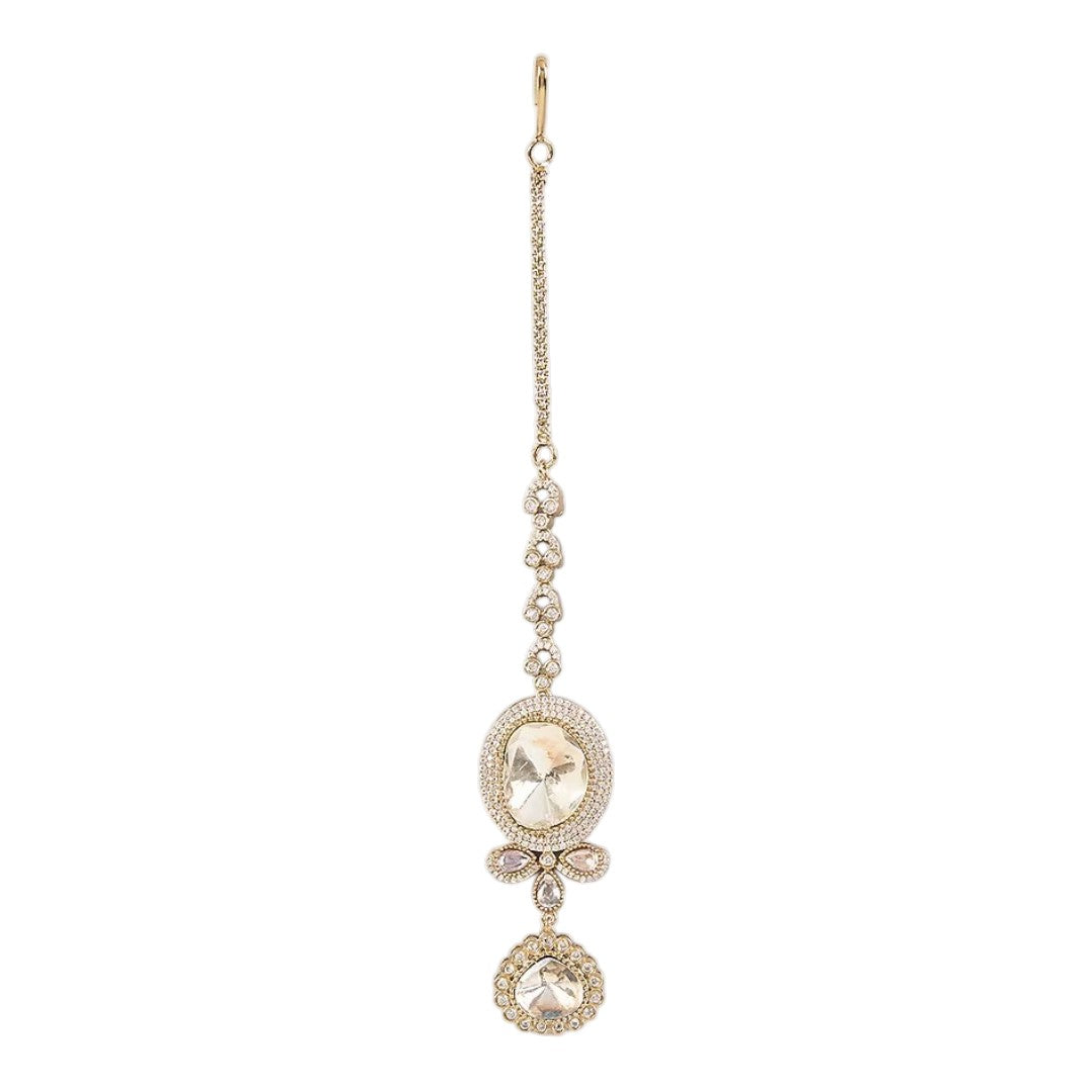 Gold-toned American Diamond oval stone maang tikka with floral crystal design and dangling charm for bridal and festive wear.