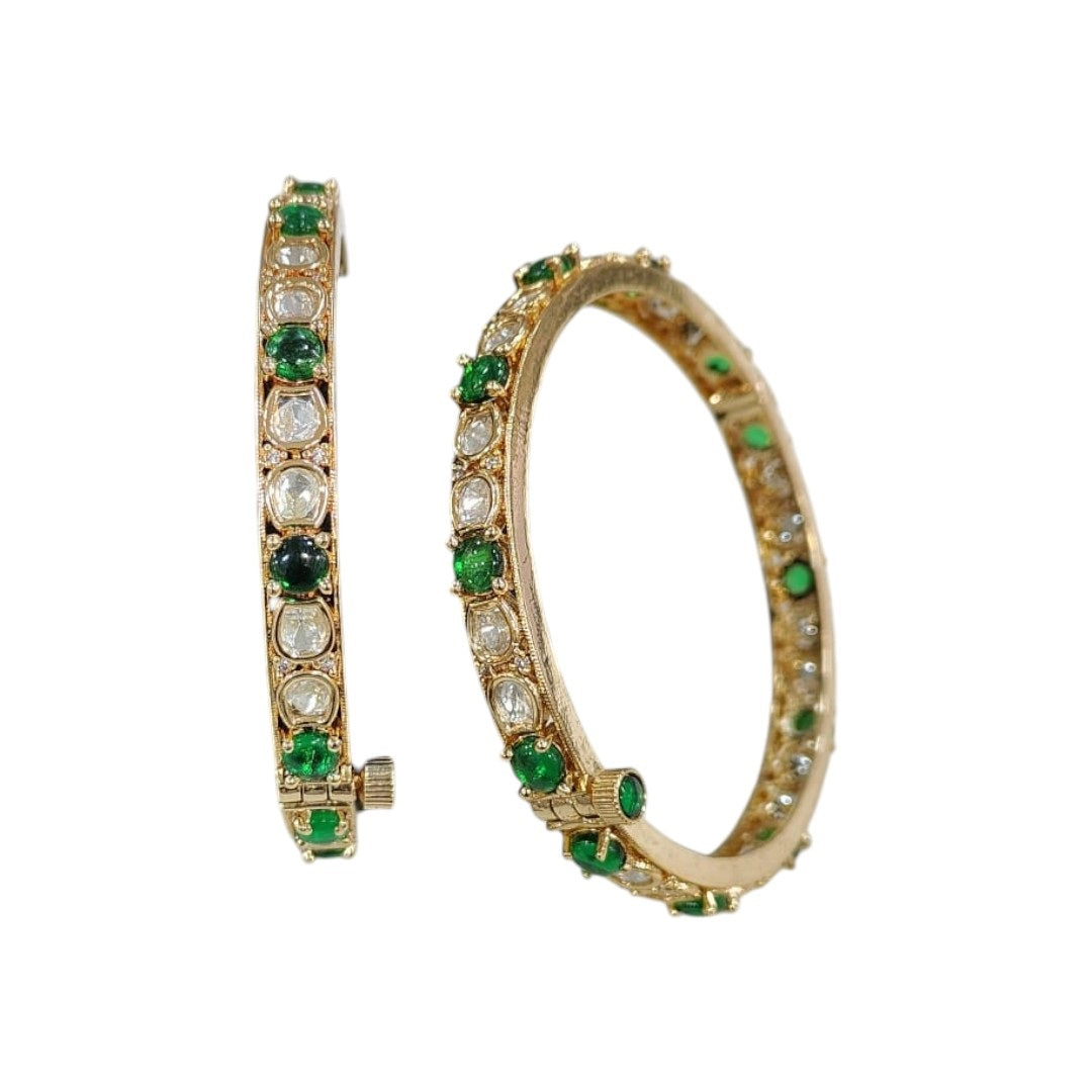 Set of gold-plated bangles adorned with alternating green and white Kundan stones, displayed on a dark green velvet roll against a white background.