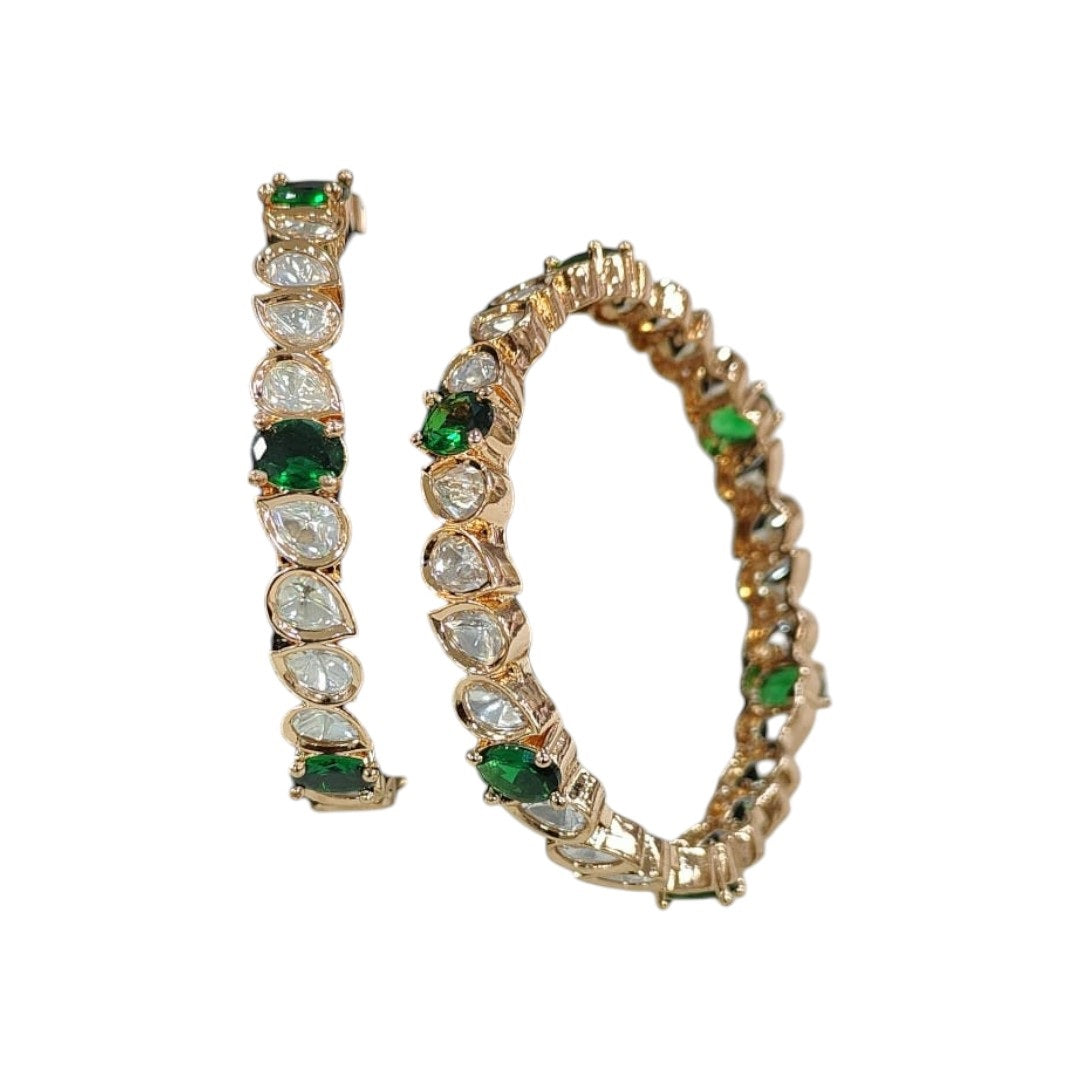 Set of gold-plated bangles with tear-drop shaped white Kundan stones and green accents displayed on a green velvet roll.
