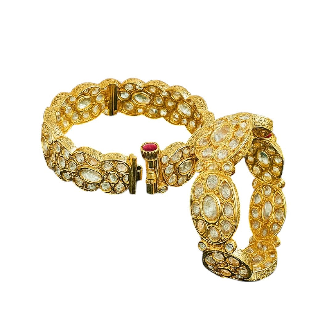 Pair of gold-plated oval Kundan stone bangles with red screw clasp detail, displayed on a green velvet cloth with pink floral background – bridal kada set for women.