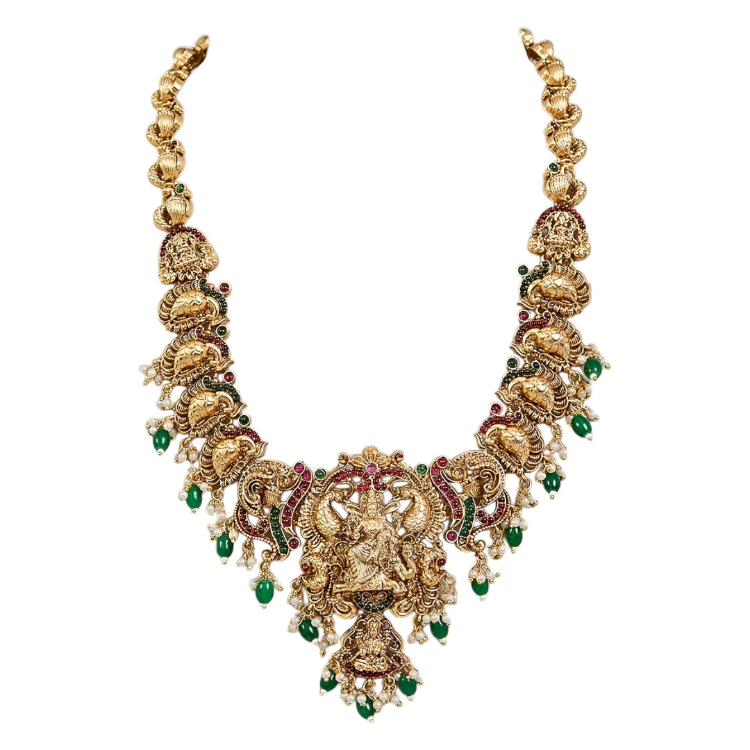 Antique gold Lakshmi temple necklace featuring traditional South Indian craftsmanship, ruby and green stone detailing, intricate deity motifs, and green bead drops for bridal and festive occasions.