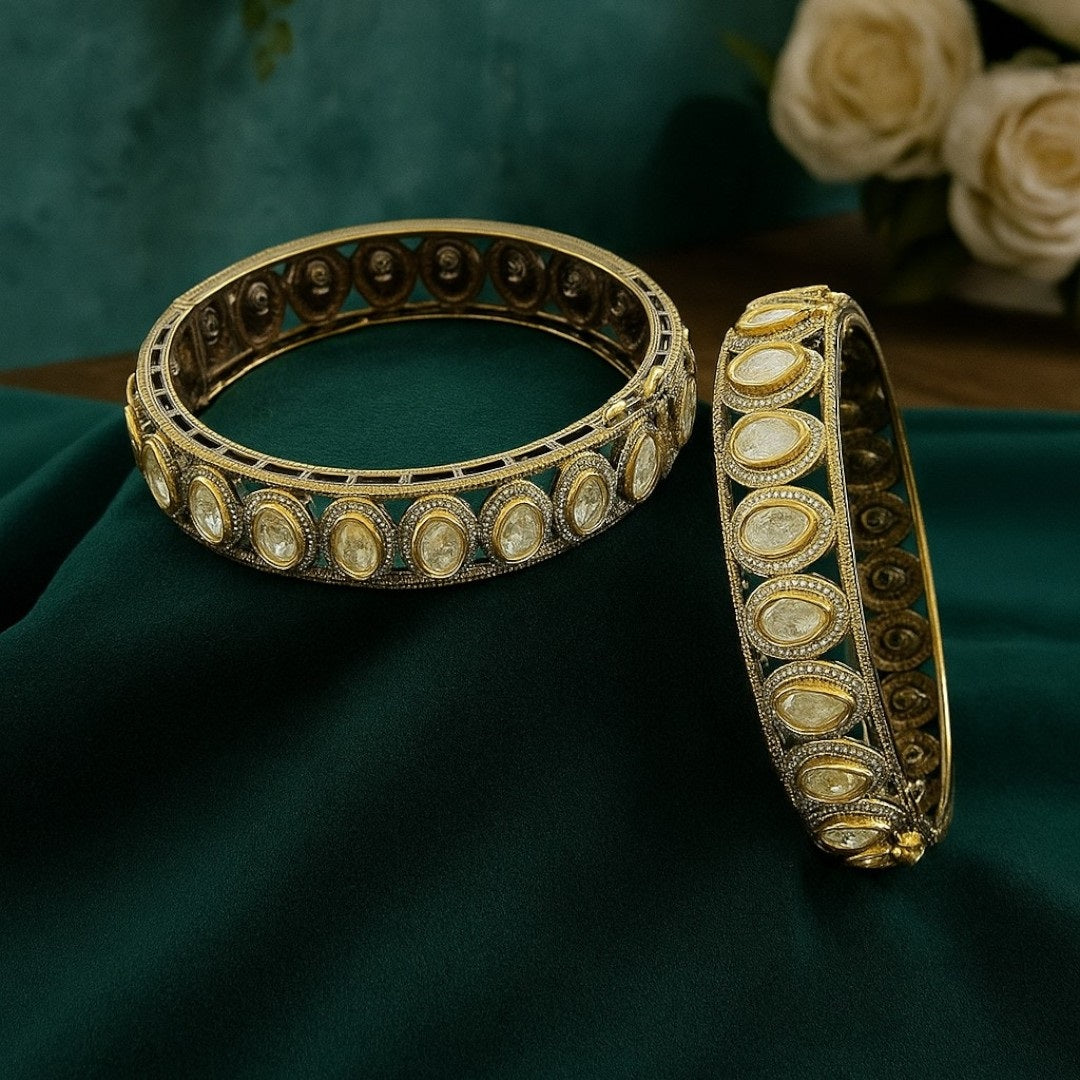 "Antique gold-plated bangles with oval polki stones in traditional Kundan style, placed on a green velvet cloth with floral background"
