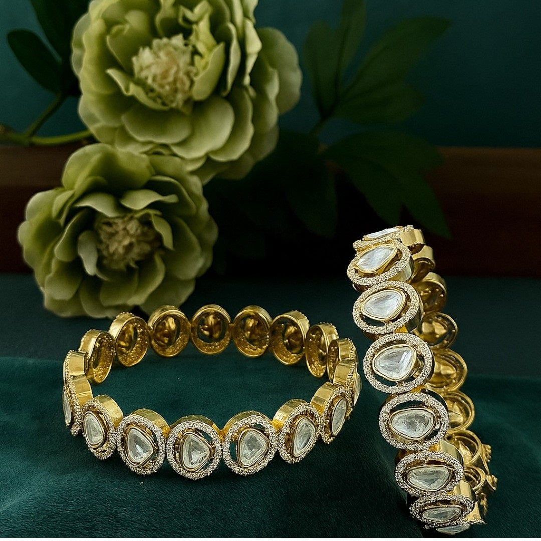 "Gold-plated bangles with teardrop Polki stones and micro-crystal detailing, displayed on green velvet with floral background"