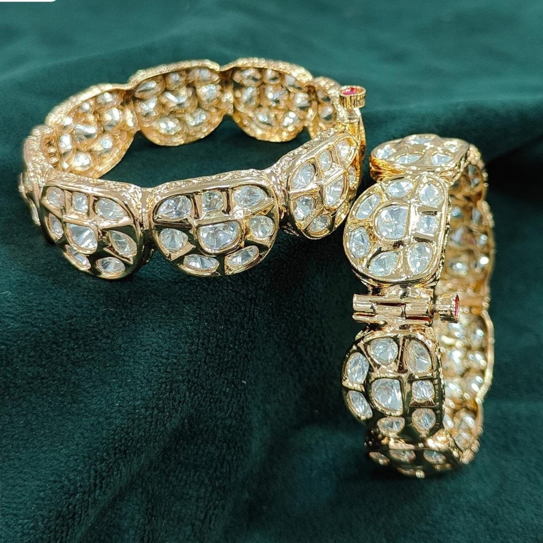 Gold plated traditional polki kundan bangles with petal-shaped panels, perfect for bridal and festive wear – displayed on a textured stone background with floral decor