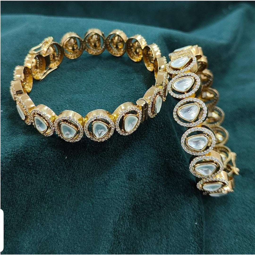 "Gold-plated bangles with teardrop Polki stones and micro-crystal detailing, displayed on green velvet with floral background"