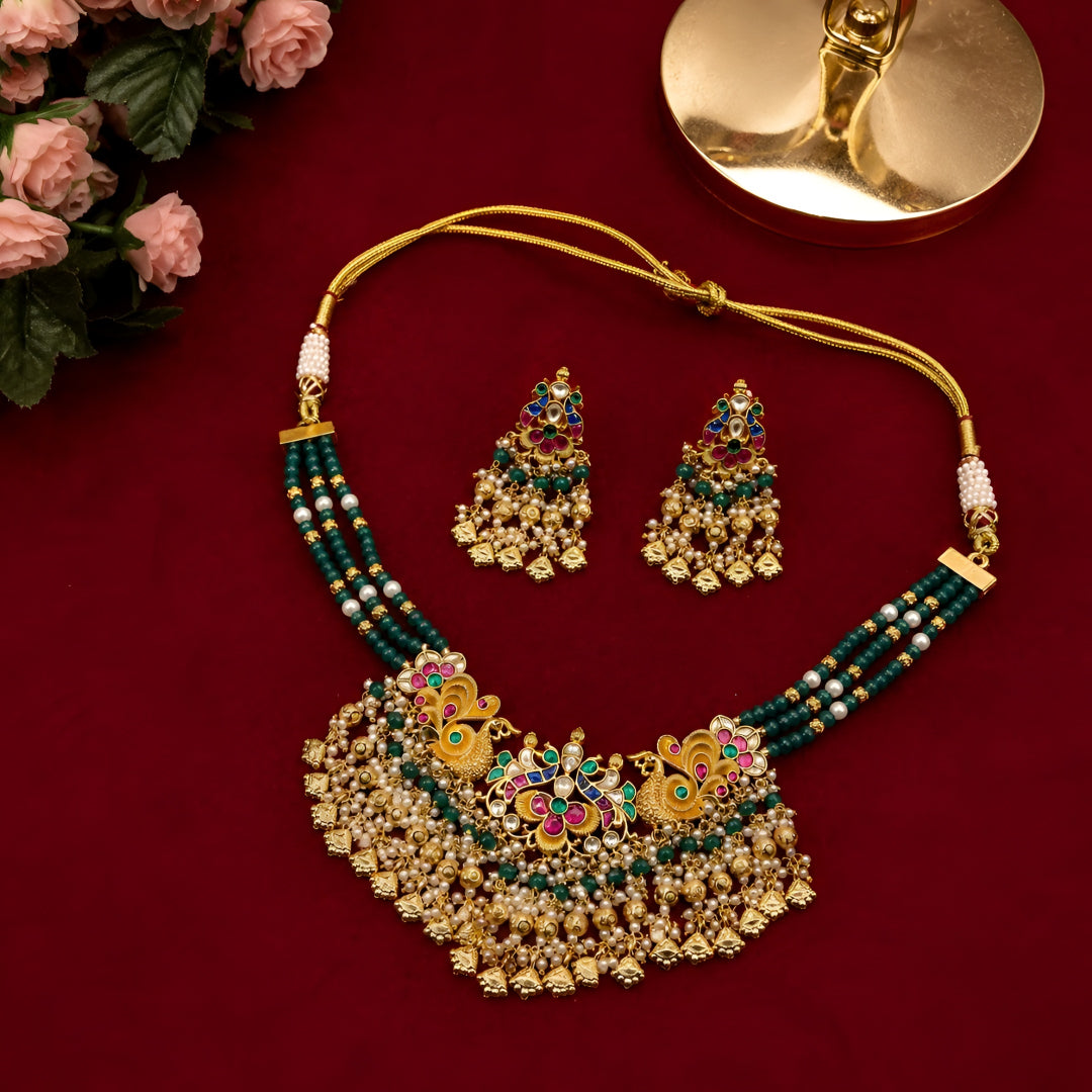 "Antique gold peacock motif necklace and earring set with green beaded strands and pearl drops, traditional temple jewellery on maroon backdrop"