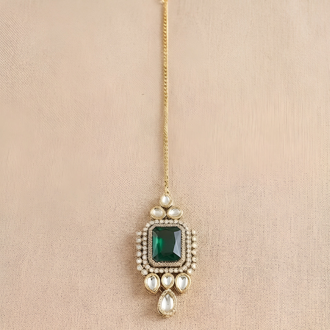 Gold maang tikka with emerald cut green stone in kundan halo setting and pearl chain, Indian bridal hair jewelry on white background