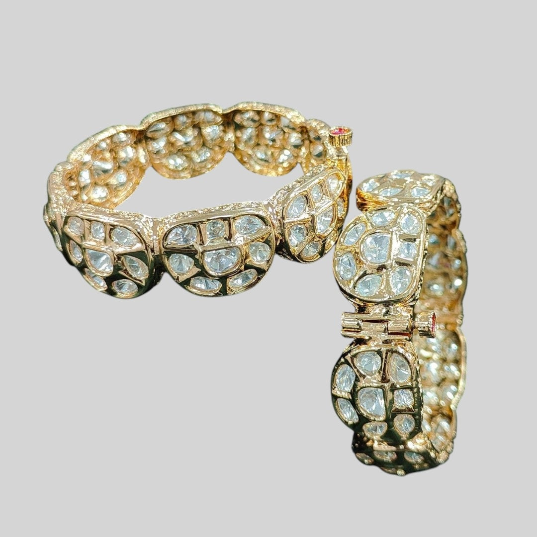 Gold plated traditional polki kundan bangles with petal-shaped panels, perfect for bridal and festive wear – displayed on a textured stone background with floral decor