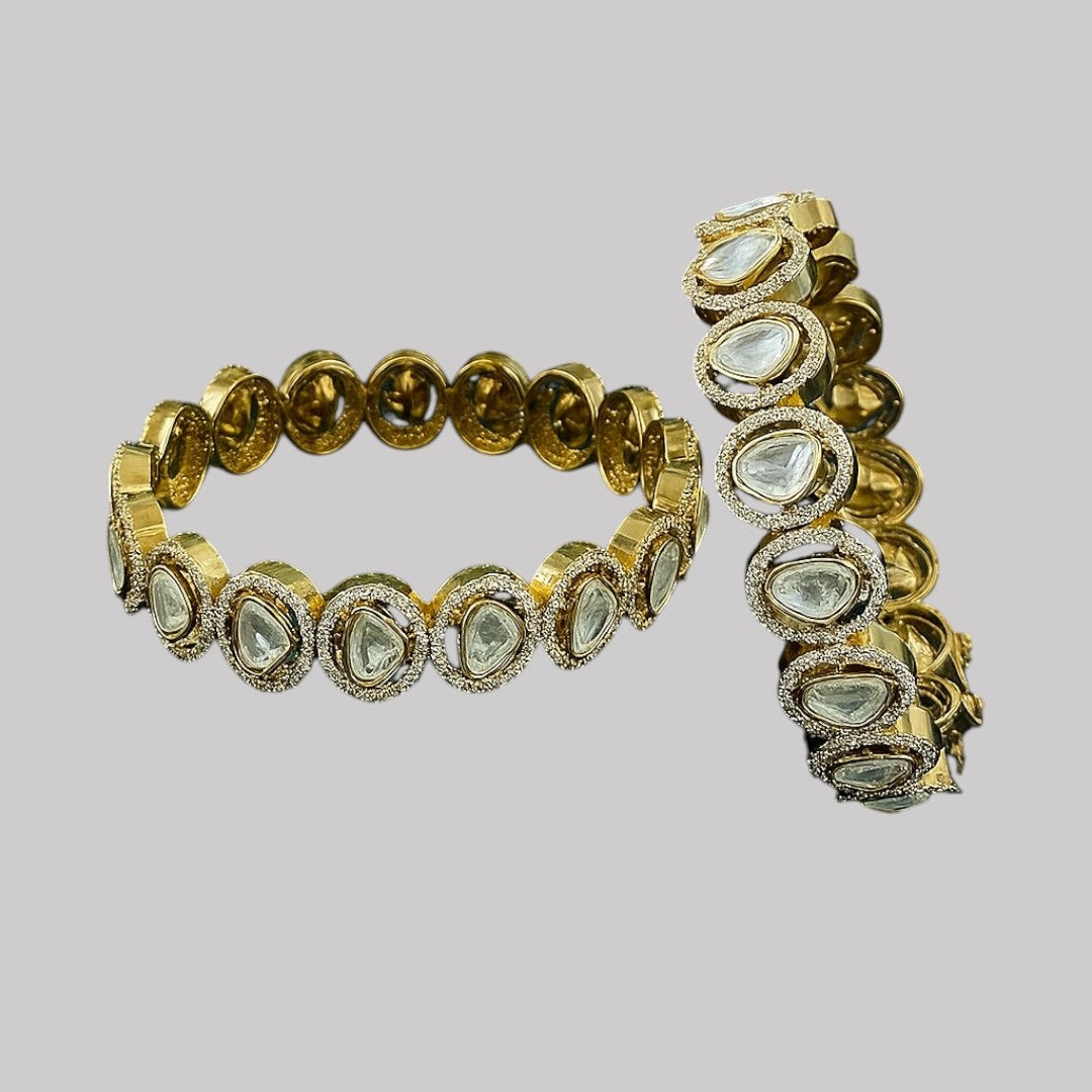 "Gold-plated bangles with teardrop Polki stones and micro-crystal detailing, displayed on green velvet with floral background"