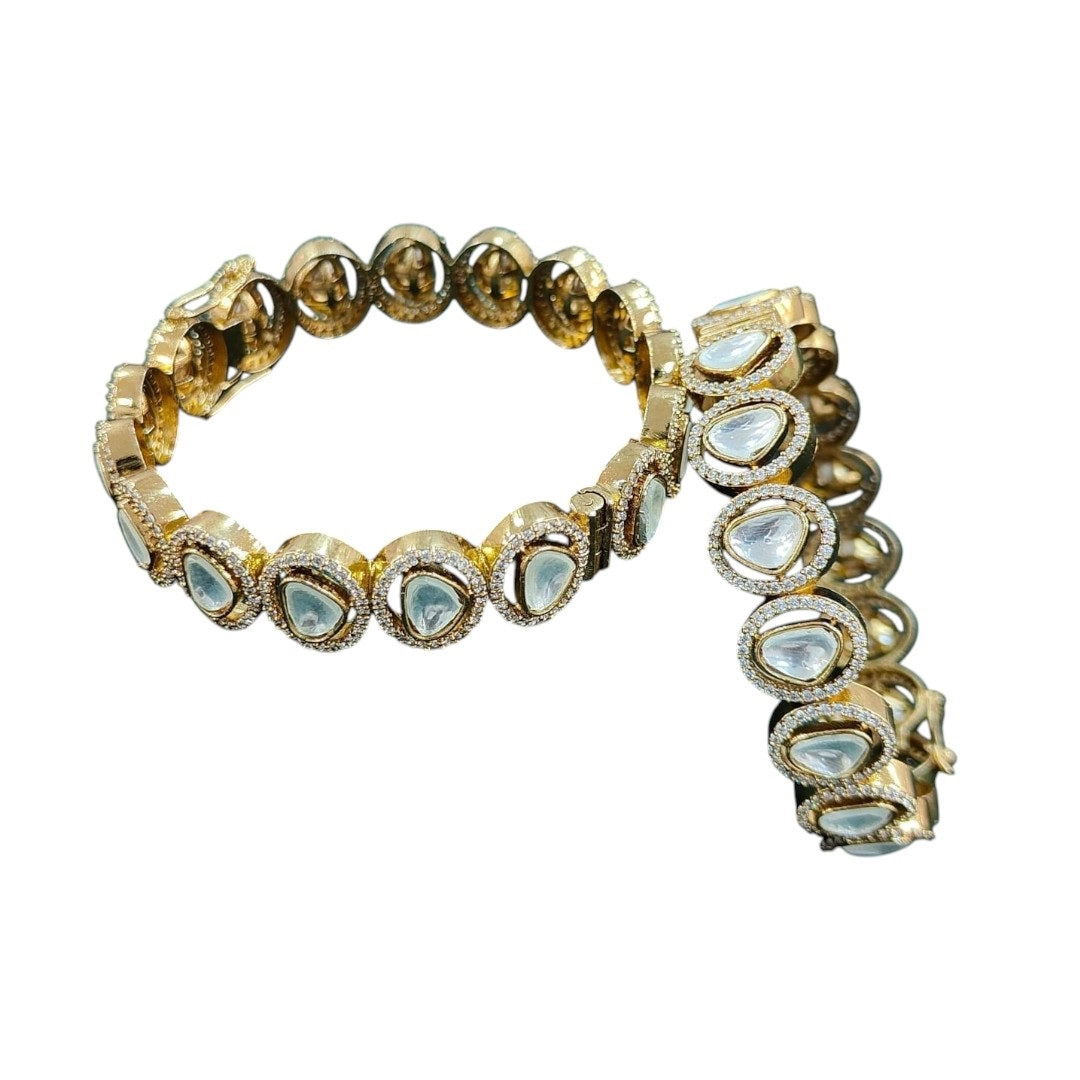 "Gold-plated bangles with teardrop Polki stones and micro-crystal detailing, displayed on green velvet with floral background"