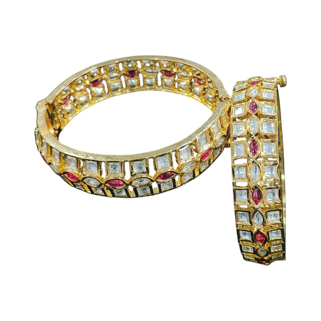 Elegant gold-plated bangles with square white stones and marquise ruby stones, placed on a marble background with yellow daisies – perfect for bridal and festive wear.