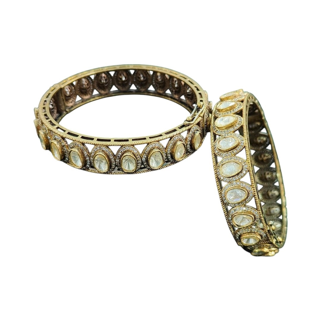 "Antique gold-plated bangles with oval polki stones in traditional Kundan style, placed on a green velvet cloth with floral background"