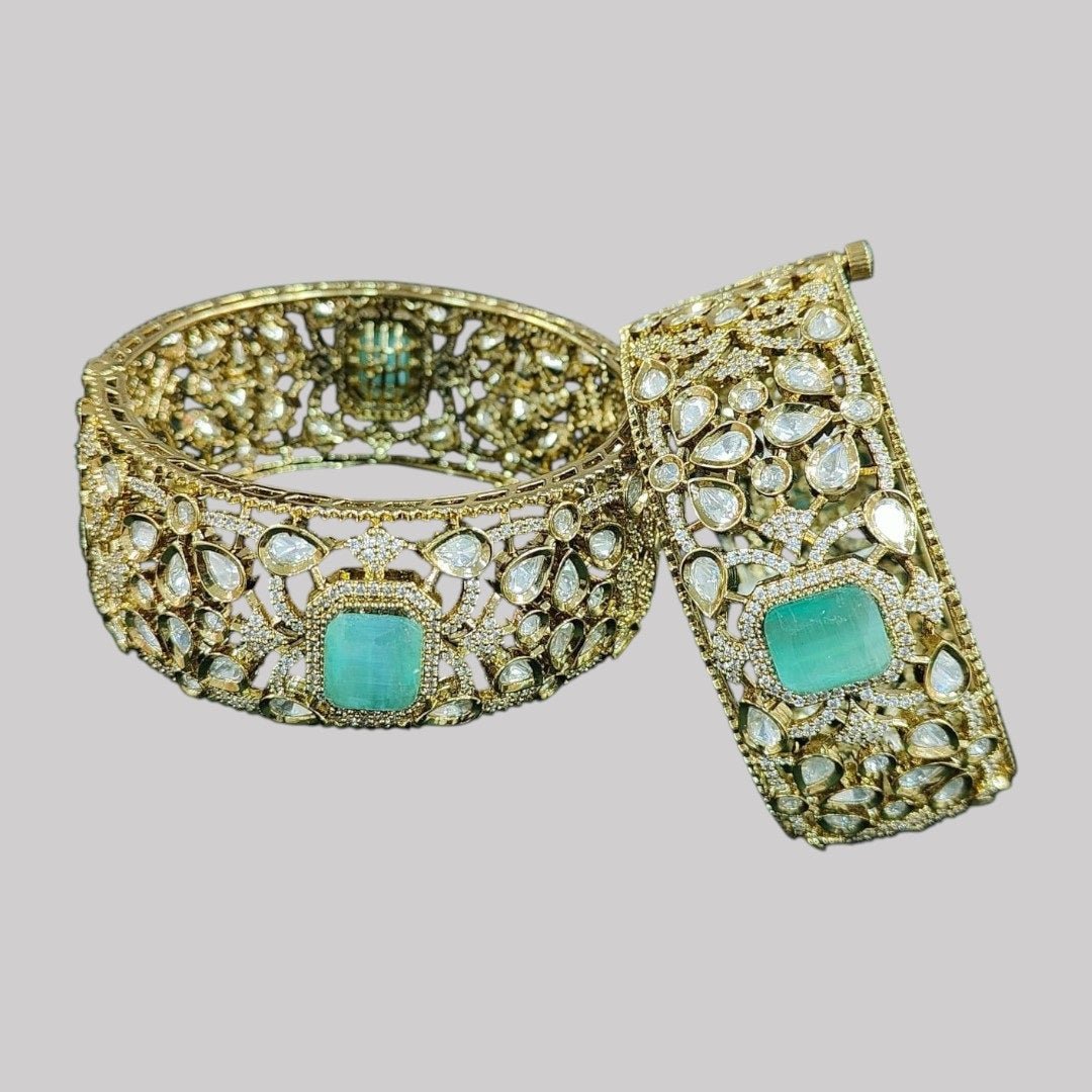 Gold - Plated Designer Broad Bangles with Mint Green Stone & Kundan Detailing - Auraa Trends - Bangles - - Auraa Trends - “Set of two gold - plated broad bangles with pastel mint green stones and intricate kundan - style design, displayed on dark green velvet fabric.”