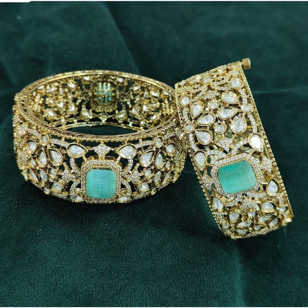 Gold - Plated Designer Broad Bangles with Mint Green Stone & Kundan Detailing - Auraa Trends - Bangles - - Auraa Trends - “Set of two gold - plated broad bangles with pastel mint green stones and intricate kundan - style design, displayed on dark green velvet fabric.”