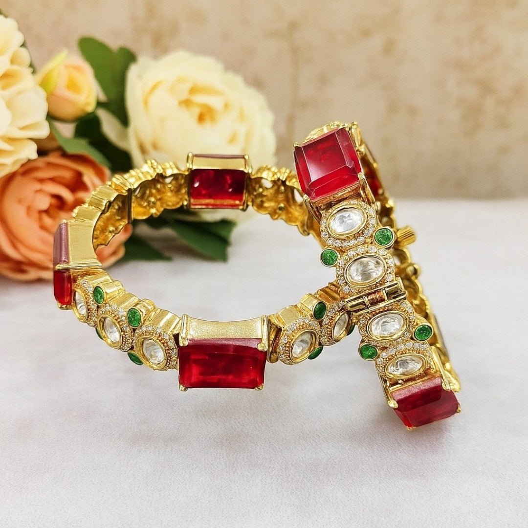 Gold - Plated Red Stone Bangles with Kundan & Green Detailing - Auraa Trends - Bangles - - Auraa Trends - “Gold - plated traditional bangles with large red stones, kundan detailing, and green enamel accents – set of 2 displayed on white background with flowers.”