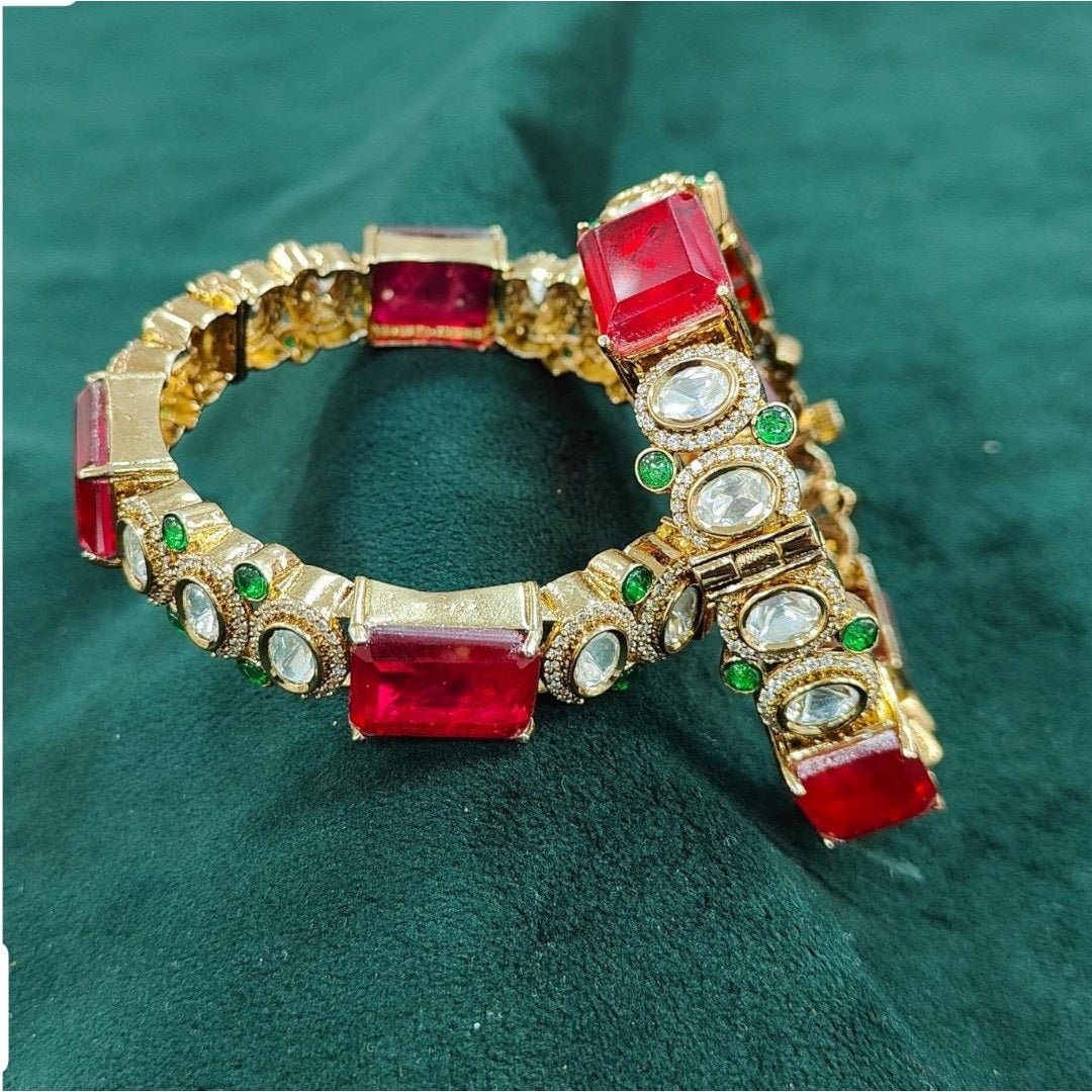 Gold - Plated Red Stone Bangles with Kundan & Green Detailing - Auraa Trends - Bangles - - Auraa Trends - “Gold - plated traditional bangles with large red stones, kundan detailing, and green enamel accents – set of 2 displayed on white background with flowers.”