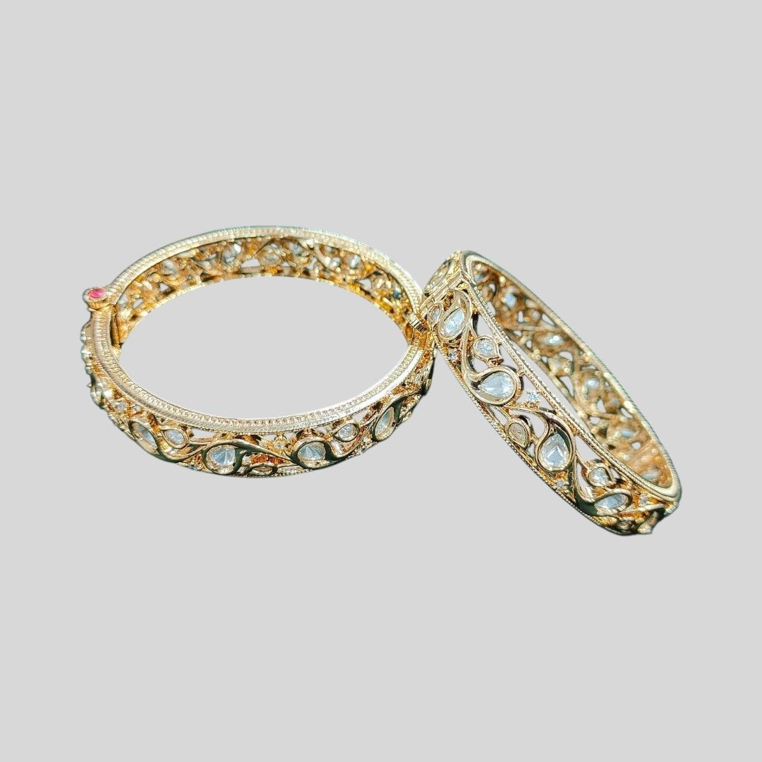 Gold - Toned Kundan Filigree Bangles with Teardrop Stones - Auraa Trends - Bangles - - Auraa Trends - โPair of gold - tone bangles with filigree cutwork and teardrop kundan stones, displayed on dark green velvet