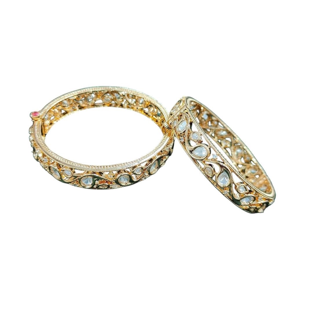 Gold - Toned Kundan Filigree Bangles with Teardrop Stones - Auraa Trends - Bangles - - Auraa Trends - โPair of gold - tone bangles with filigree cutwork and teardrop kundan stones, displayed on dark green velvet