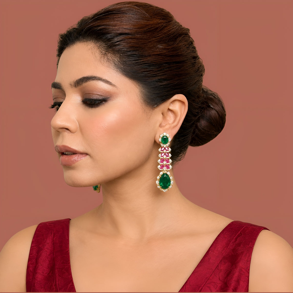 Gold-tone American diamond long drop earrings with emerald-green oval tops, ruby-pink marquise leaf rows and large emerald-green pear drops on dark green velvet