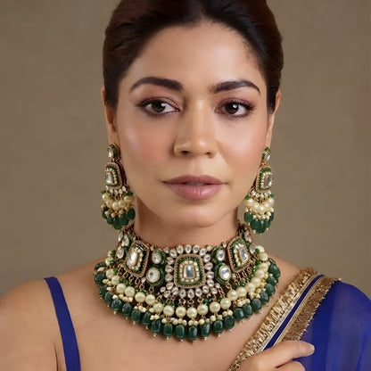 Gold kundan choker necklace set with green meenakari motifs, pearl and green bead drops and matching chandelier earrings on brown bust