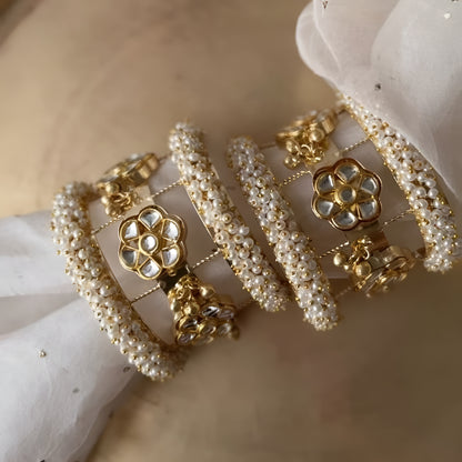 Gold-plated Kundan pearl bangles set for women with floral motifs, faux pearl beadwork, and hanging jhumki charms.