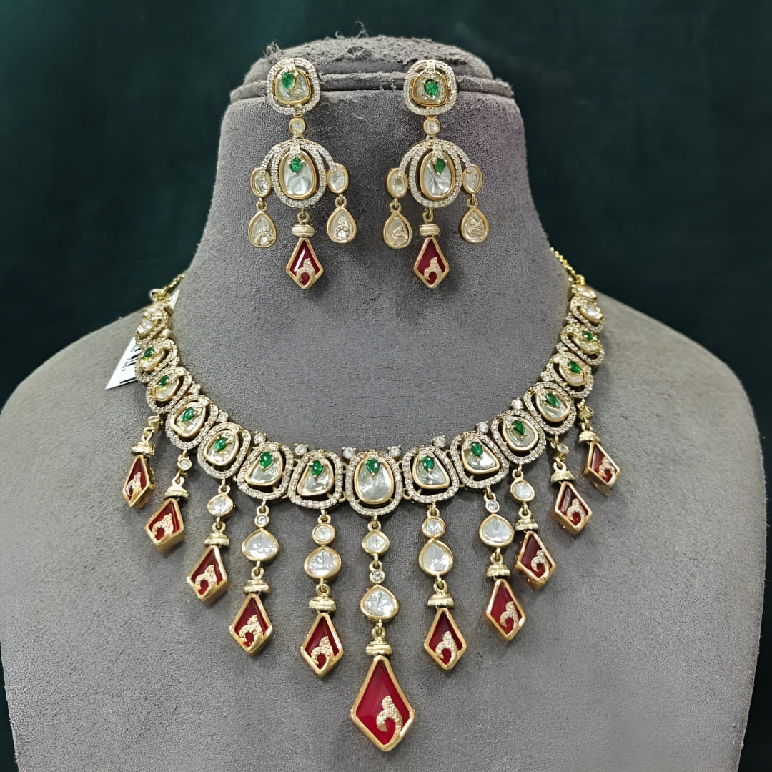 Gold-tone kundan necklace set with red kite-shaped drops, green accent stones and matching chandelier earrings on a grey display bust
