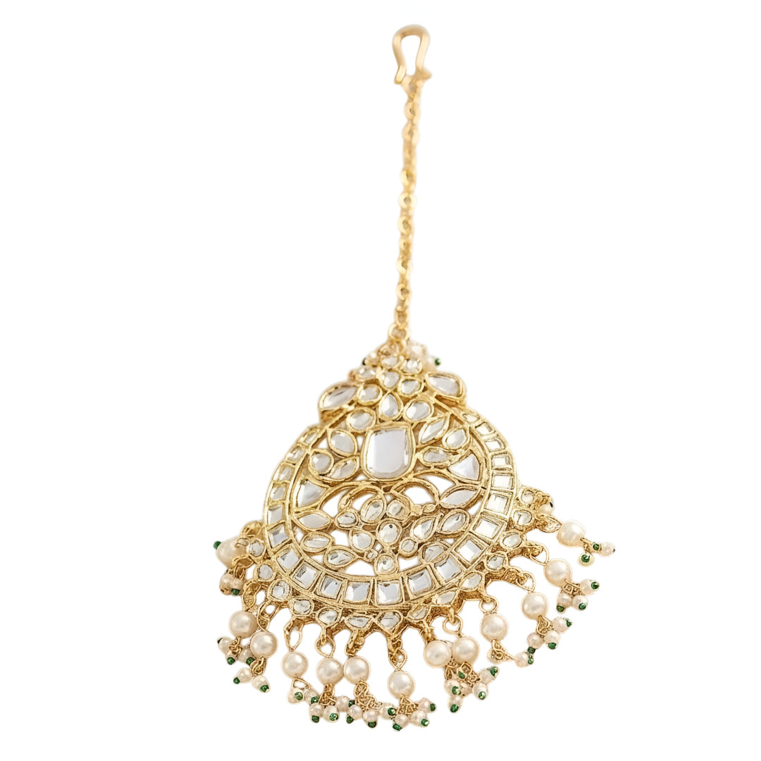Gold kundan maang tikka with pearl and green bead tassels, traditional Indian bridal hair jewelry on white background