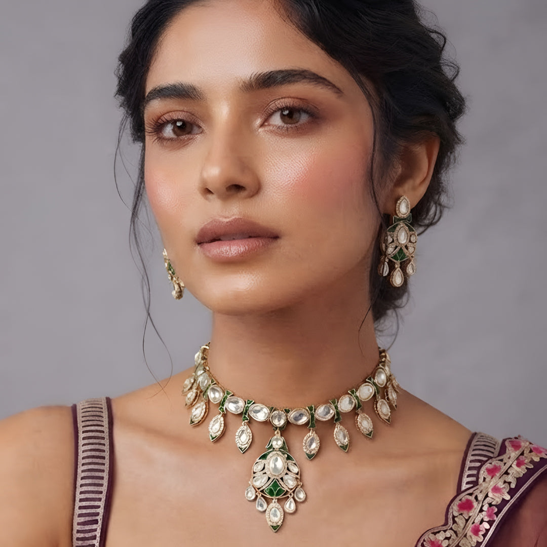 Gold-tone green meenakari kundan necklace set with round centre pendant, leaf-shaped drops and matching drop earrings on a grey display bust