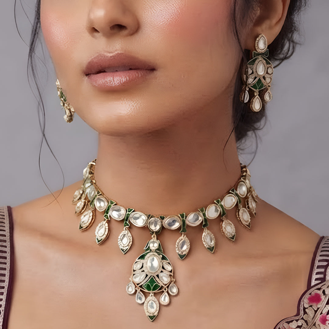 Gold-tone green meenakari kundan necklace set with round centre pendant, leaf-shaped drops and matching drop earrings on a grey display bust