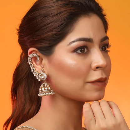 Gold plated peacock design jhumka earrings with American diamonds and pearl drops on white background