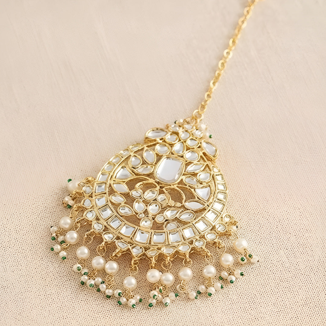 Gold kundan maang tikka with pearl and green bead tassels, traditional Indian bridal hair jewelry on white background