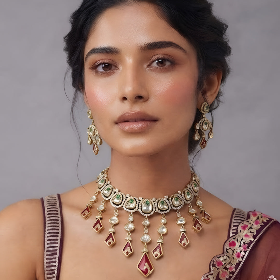 Gold-tone kundan necklace set with red kite-shaped drops, green accent stones and matching chandelier earrings on a grey display bust