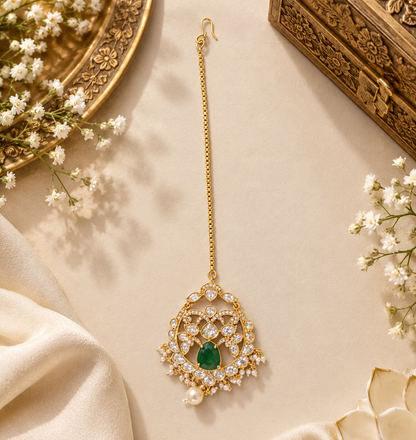 Gold-plated kundan polki style maang tikka with emerald green centre stone, clear floral medallion, pearl fringe, pearl drop and box chain with hook