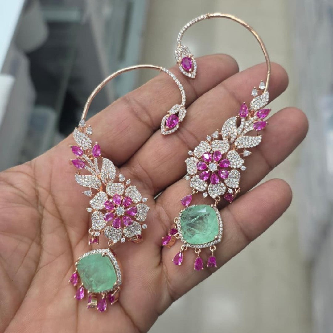 Rose gold American diamond ear cuff earrings with ruby pink pear stones and mint green cushion-cut drops, held in hand