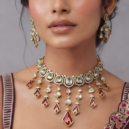 Gold-tone kundan necklace set with red kite-shaped drops, green accent stones and matching chandelier earrings on a grey display bust