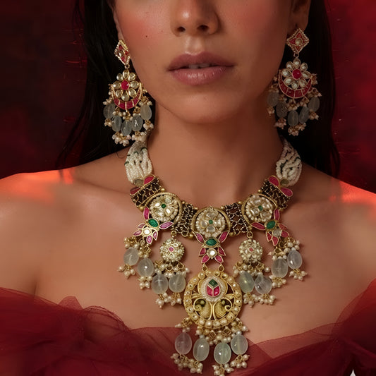 "Antique gold Kundan necklace and earring set with multi-strand pearl beading, ruby-green stone work, peacock detail and green bead drops, traditional jewellery on maroon backdrop"