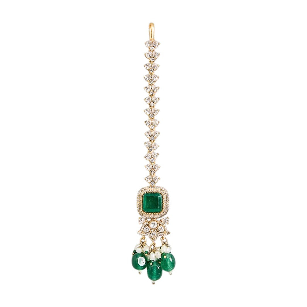 "Gold-toned maang tikka with layered polki stones, emerald green floral accents and teardrop pendant, traditional Indian bridal jewelry"