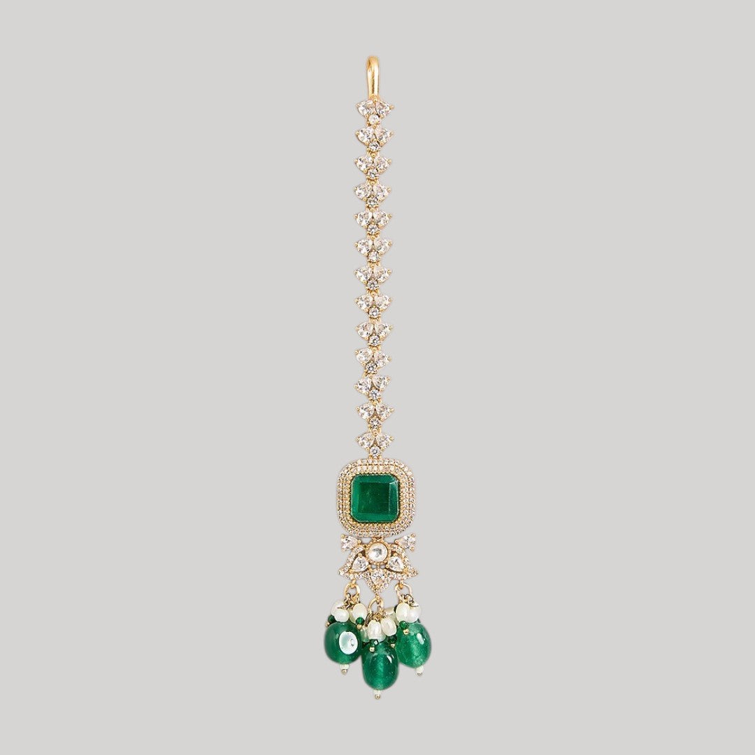 "Gold-toned maang tikka with layered polki stones, emerald green floral accents and teardrop pendant, traditional Indian bridal jewelry"
