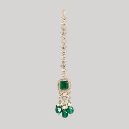 "Gold-toned maang tikka with layered polki stones, emerald green floral accents and teardrop pendant, traditional Indian bridal jewelry"