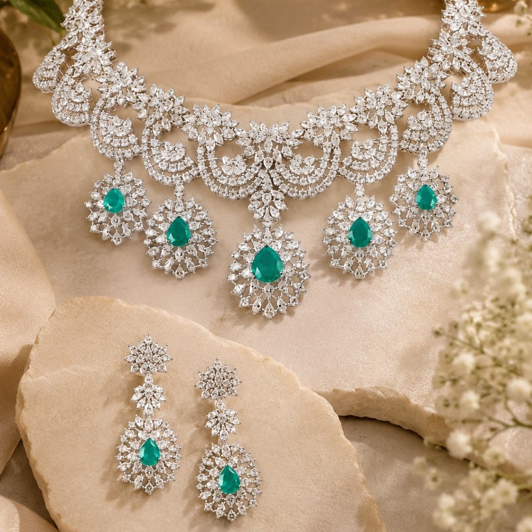 "Silver rhodium-plated bridal necklace set with white American diamonds and green emerald drop stones, paired with matching floral drop earrings"