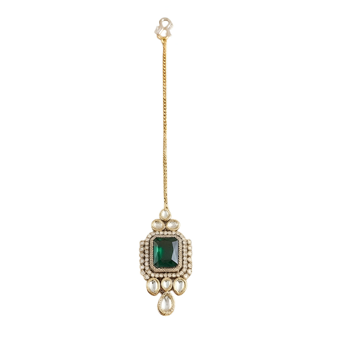 Gold maang tikka with emerald cut green stone in kundan halo setting and pearl chain, Indian bridal hair jewelry on white background