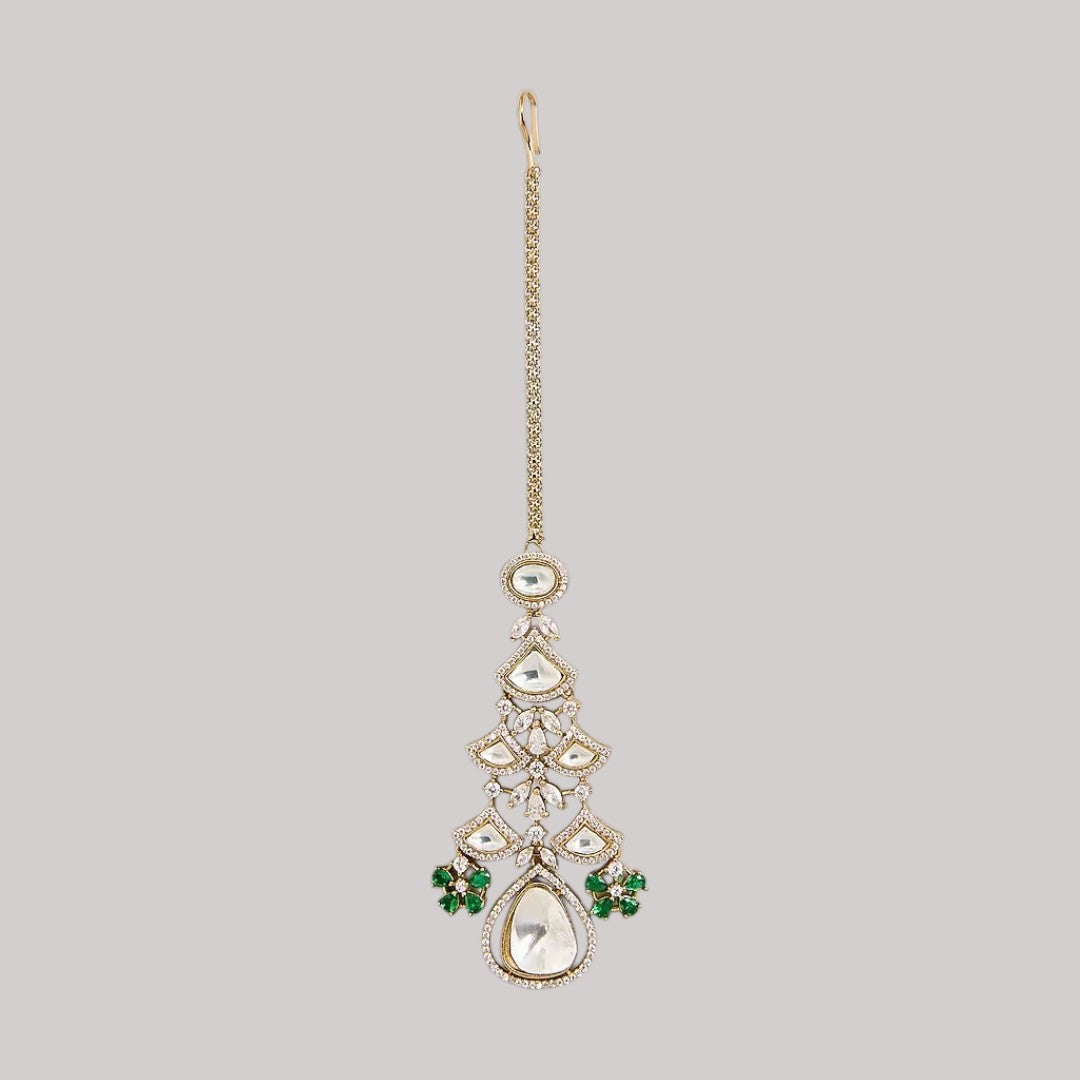 "Gold-toned maang tikka with layered polki stones, emerald green floral accents and teardrop pendant, traditional Indian bridal jewelry"