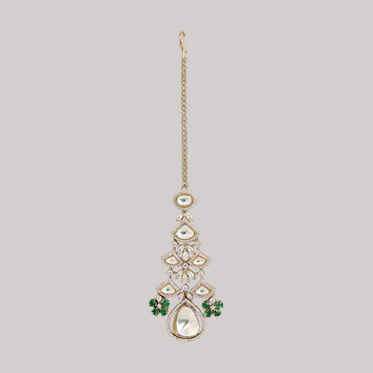 "Gold-toned maang tikka with layered polki stones, emerald green floral accents and teardrop pendant, traditional Indian bridal jewelry"