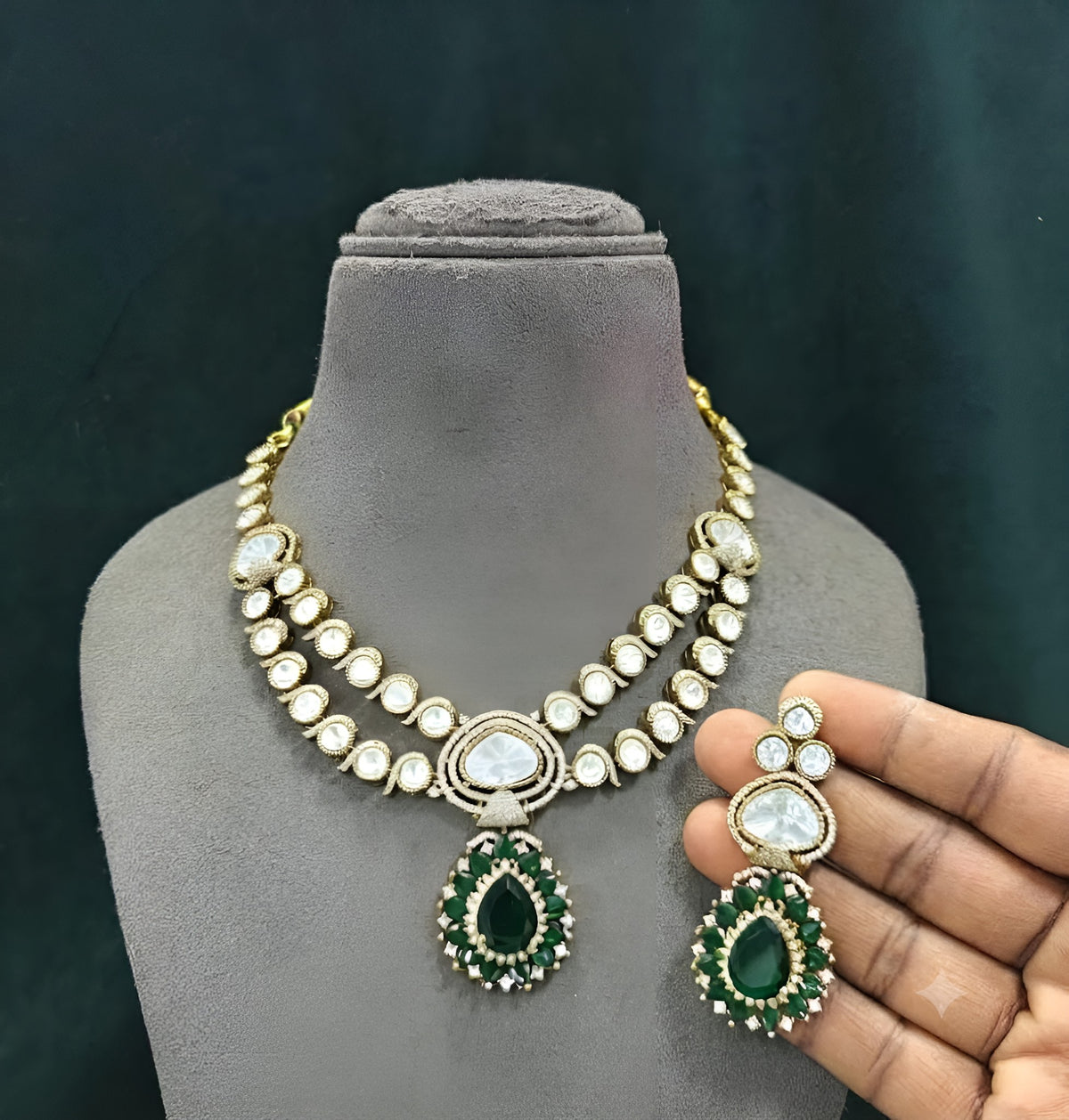 Antique gold two-strand polki kundan necklace with emerald green teardrop pendant on a display bust